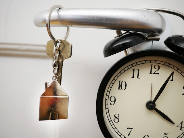 a key in the door with model of a home as a keyring and a clock on the door knob